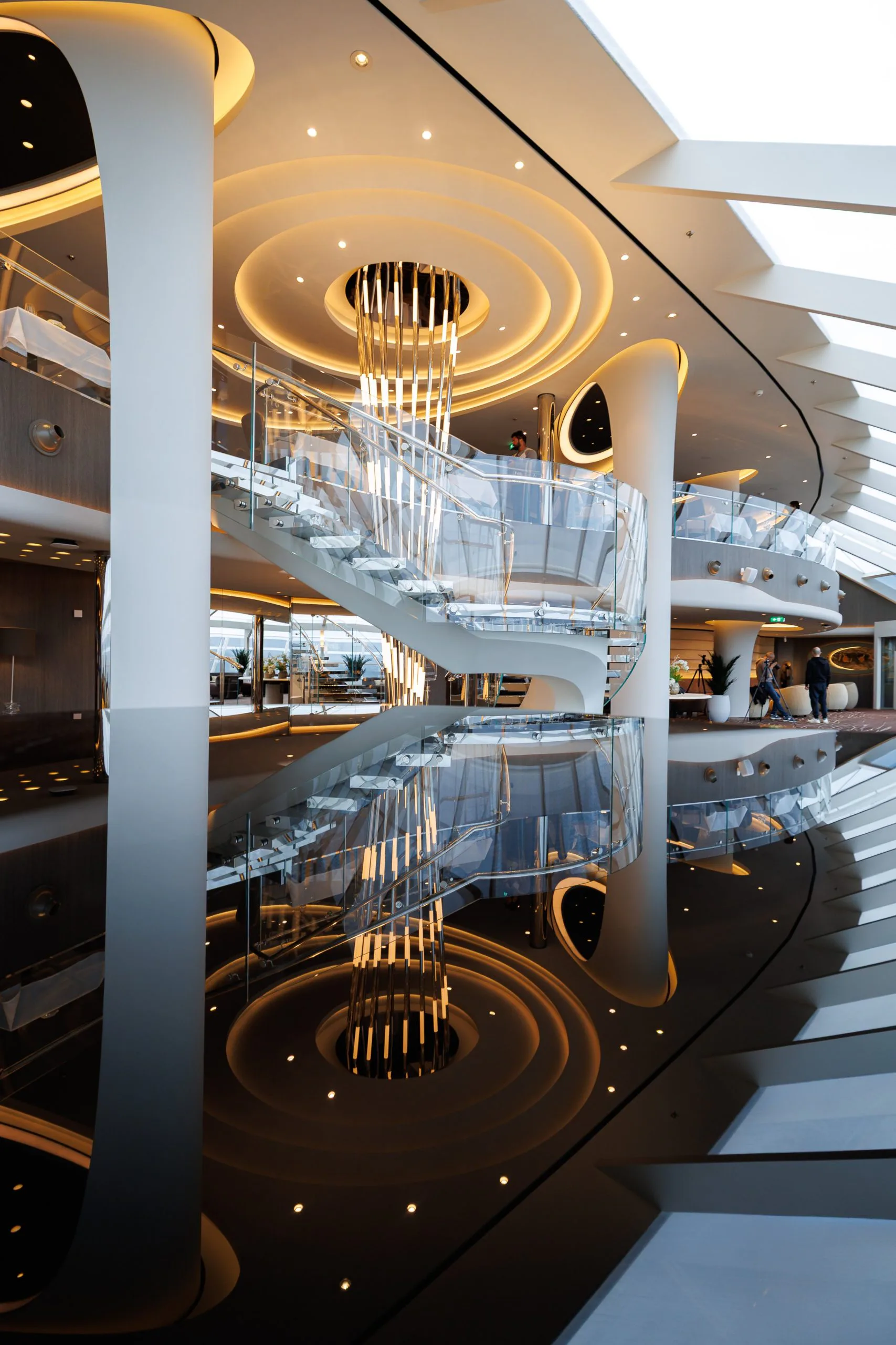 Interior moderne d'un bâtiment avec escalier central en spirale, éclairage design, murs blancs, et éléments architecturaux futuristes, avec une reflection parfaite au sol.