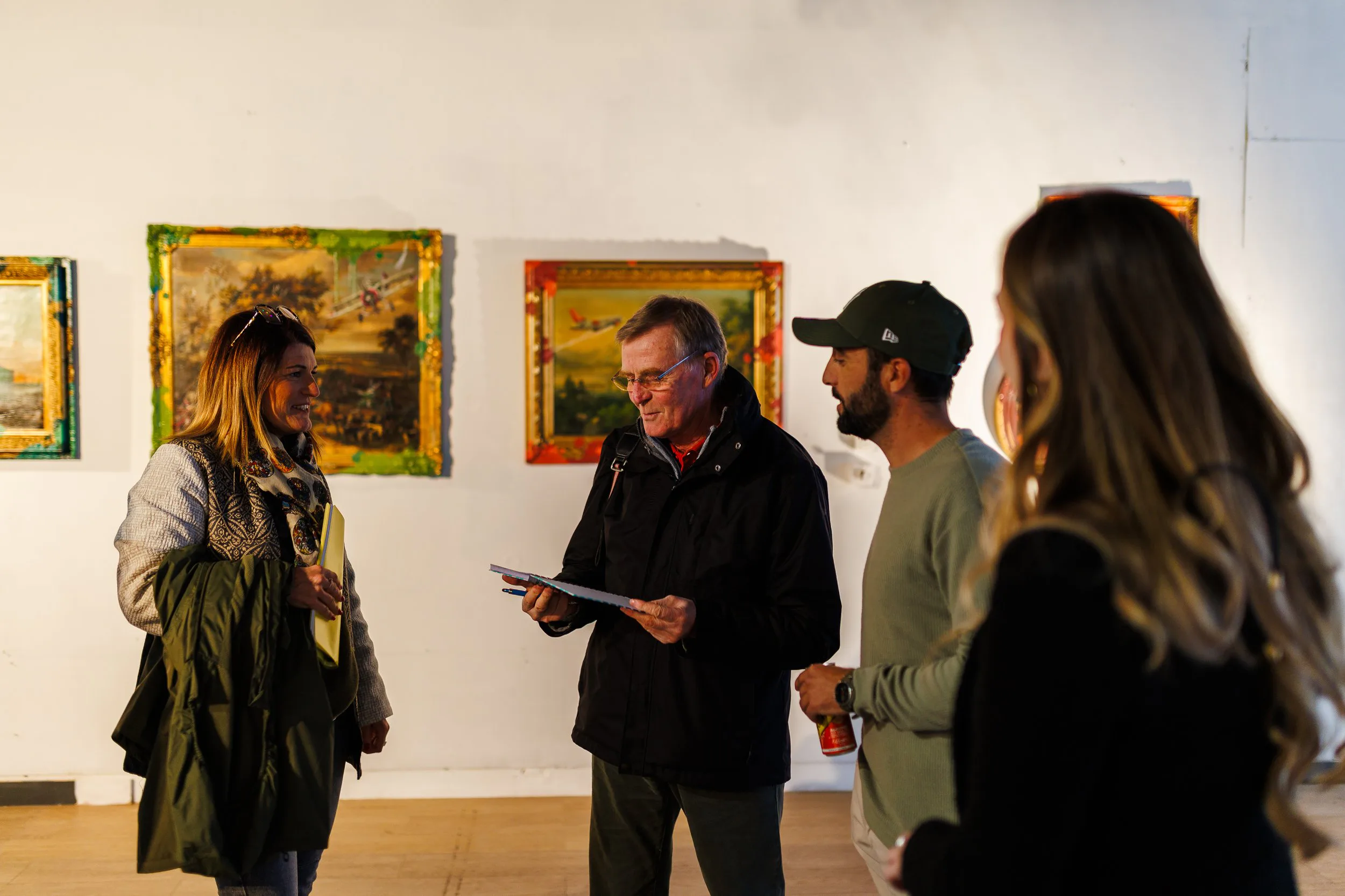 Groupe de quatre personnes discutant dans une galerie d'art avec des tableaux en arrière-plan.