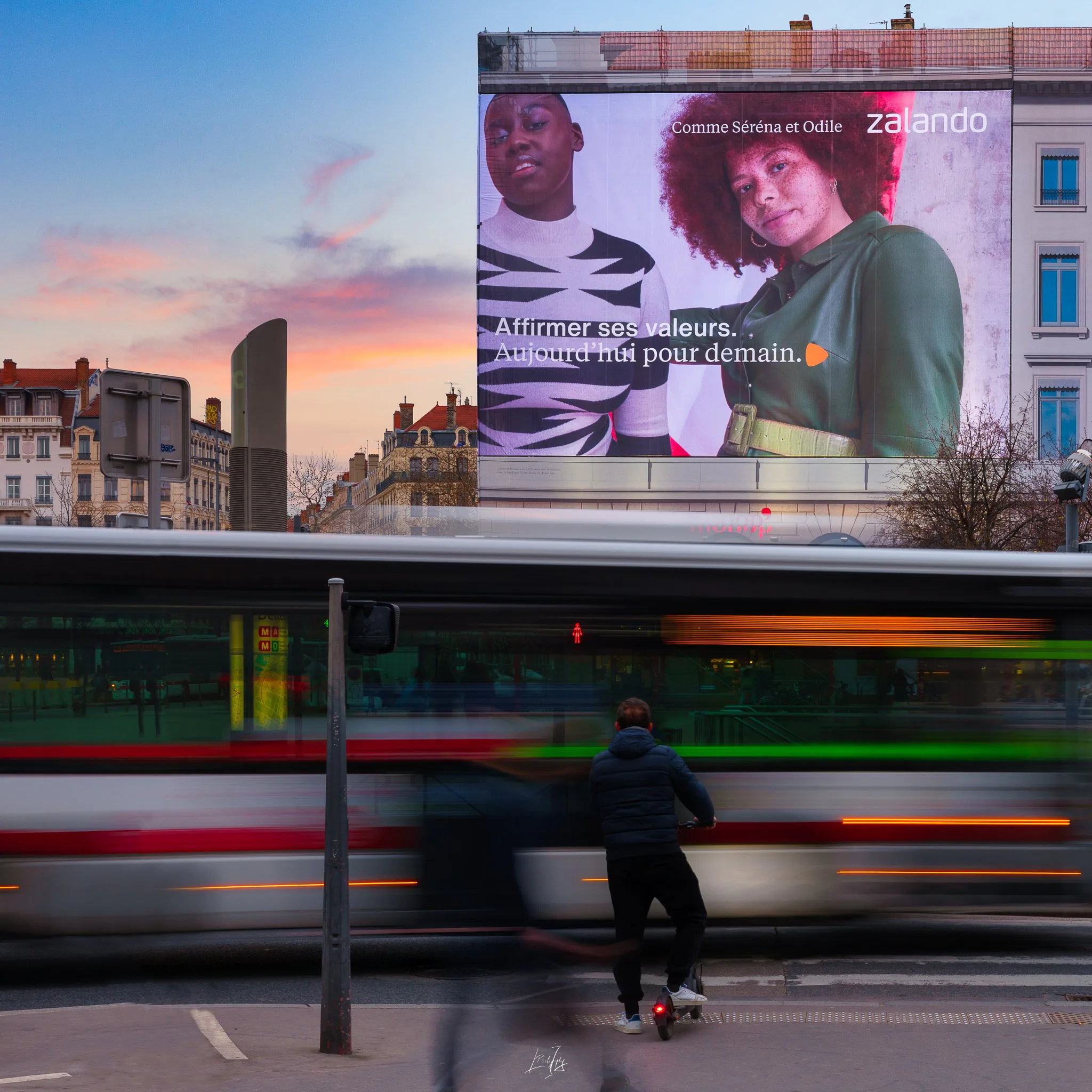 Bâche publicitaire géante au coucher du soleil, tramway au premier plan, à Lyon