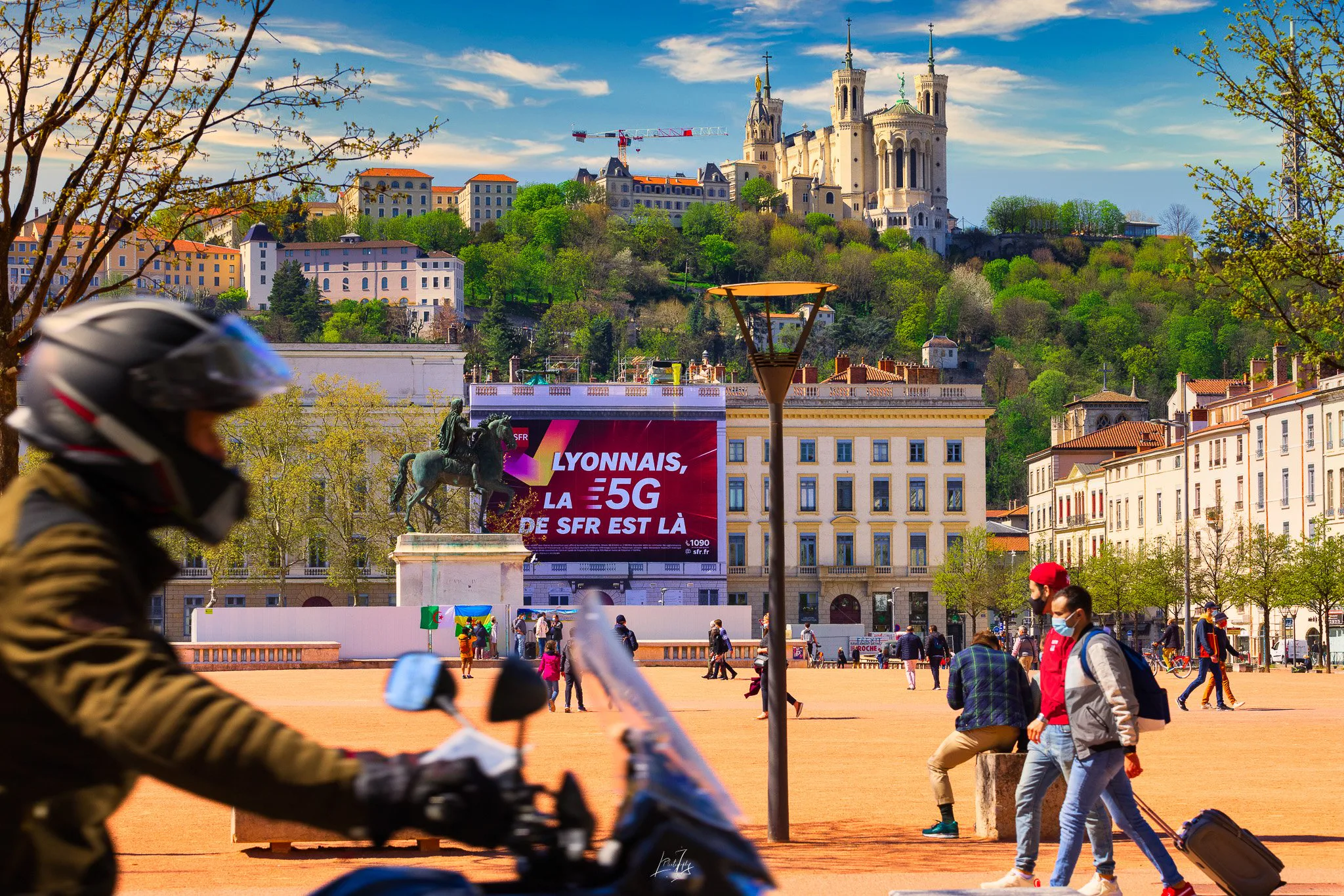 Motard devant la bâche SFR place Bellecour, Fourvière en arrière-plan