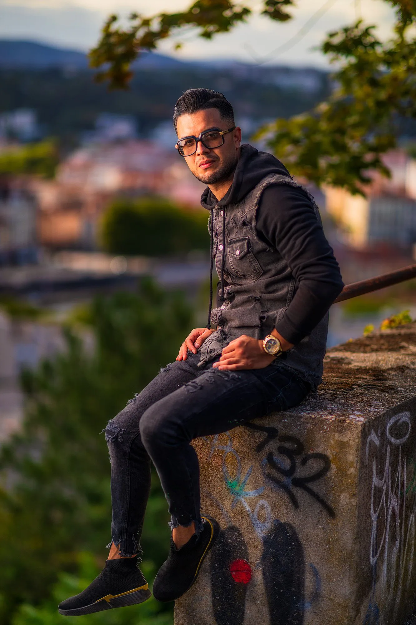 Portrait lifestyle d’Alaa assis sur un muret, vue sur la ville