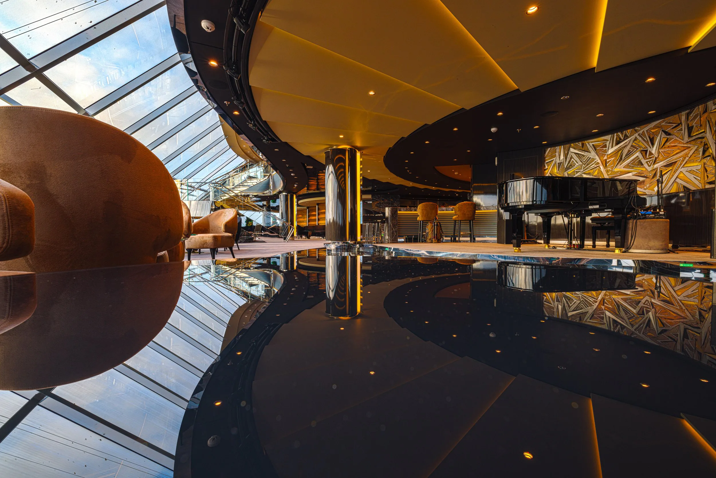Intérieur d'un lounge avec un piano noir, des fauteuils en cuir, un mur avec un motif géométrique, une grande baie vitrée laissant entrer la lumière naturelle, et un sol réfléchissant.