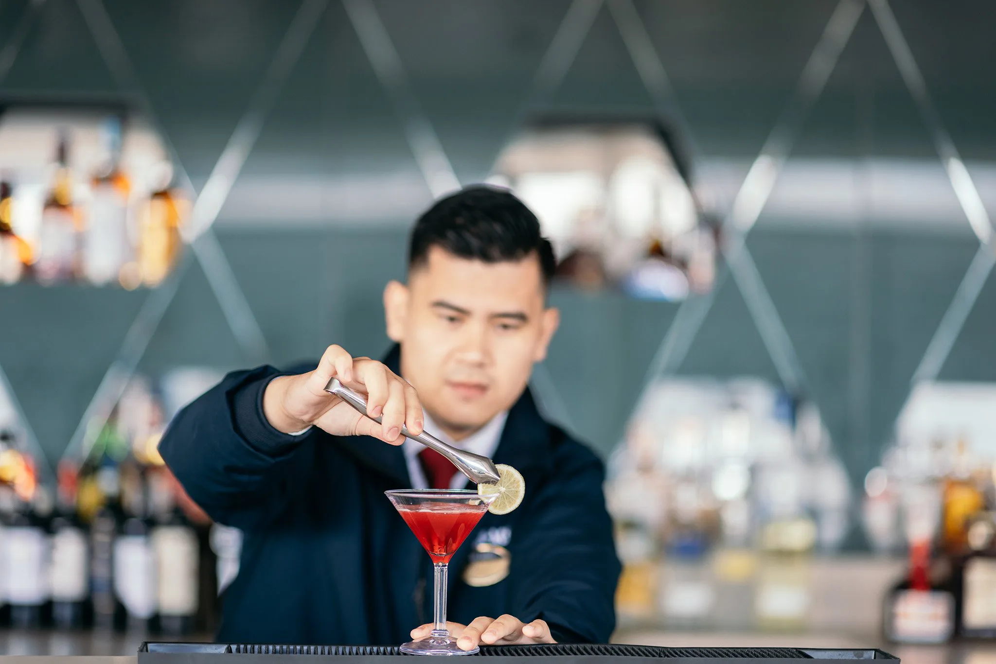 Un barman prépare un cocktail rouge dans un verre à martini, en le garnissant d'une tranche de citron, dans un bar moderne.