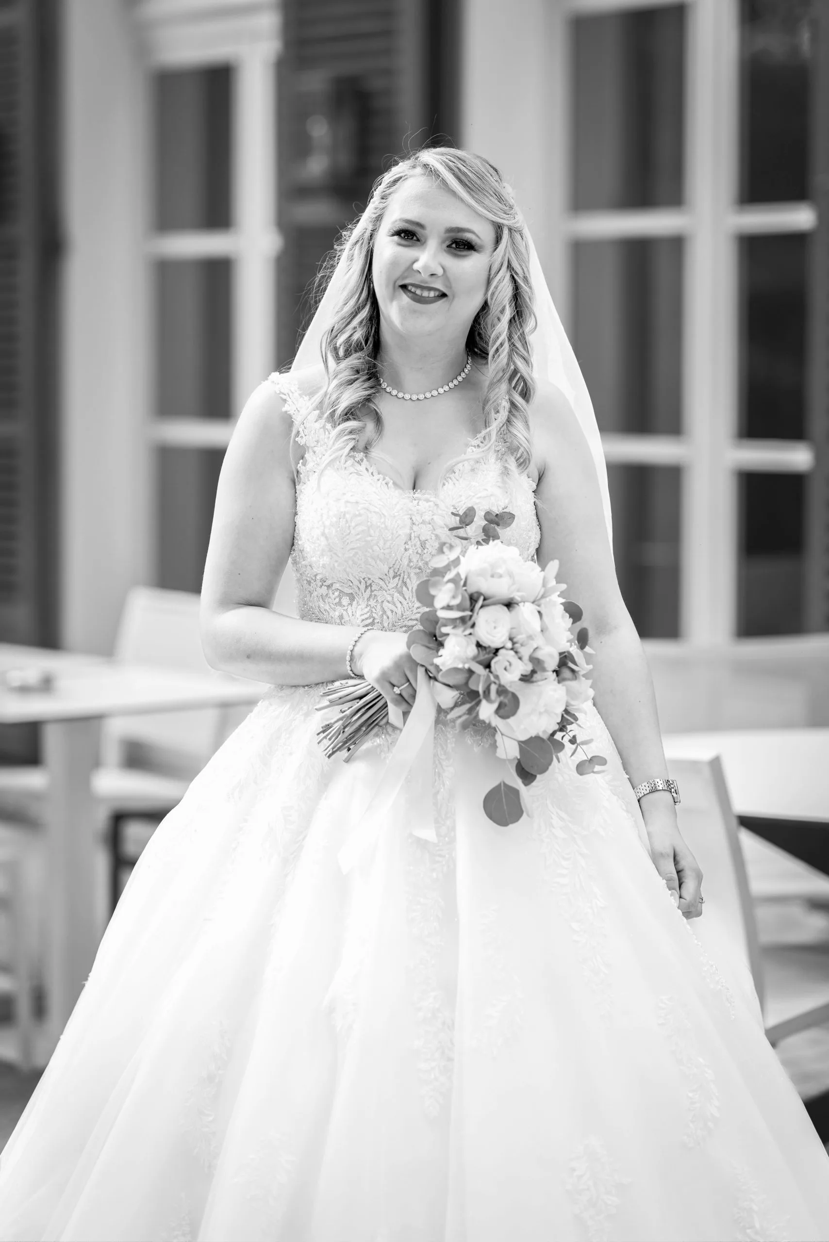 Portrait de la mariée en noir et blanc devant la demeure, bouquet à la main
