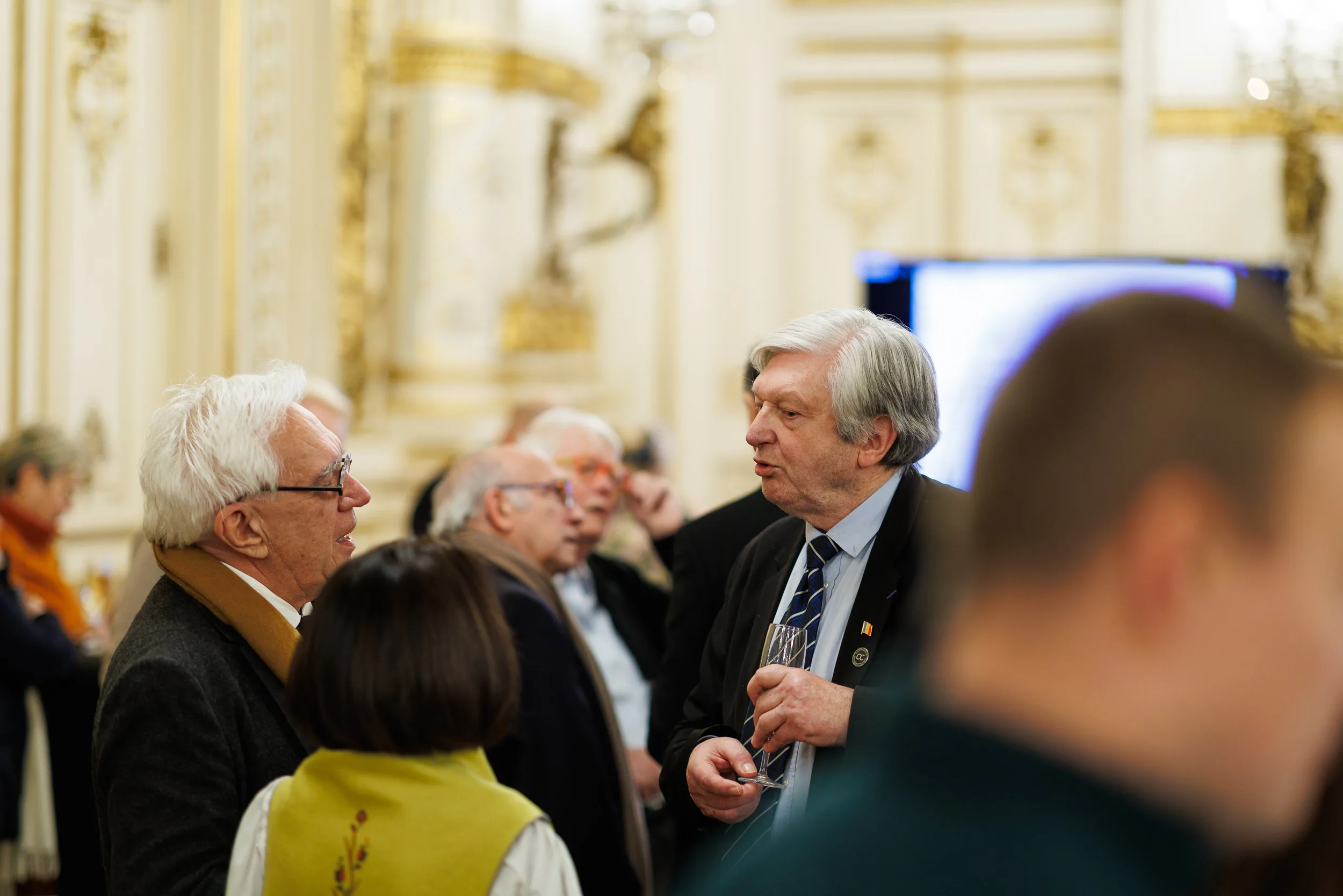 Groupe de personnes discutant lors d'un événement formel dans un salon luxueux avec décoration dorée.