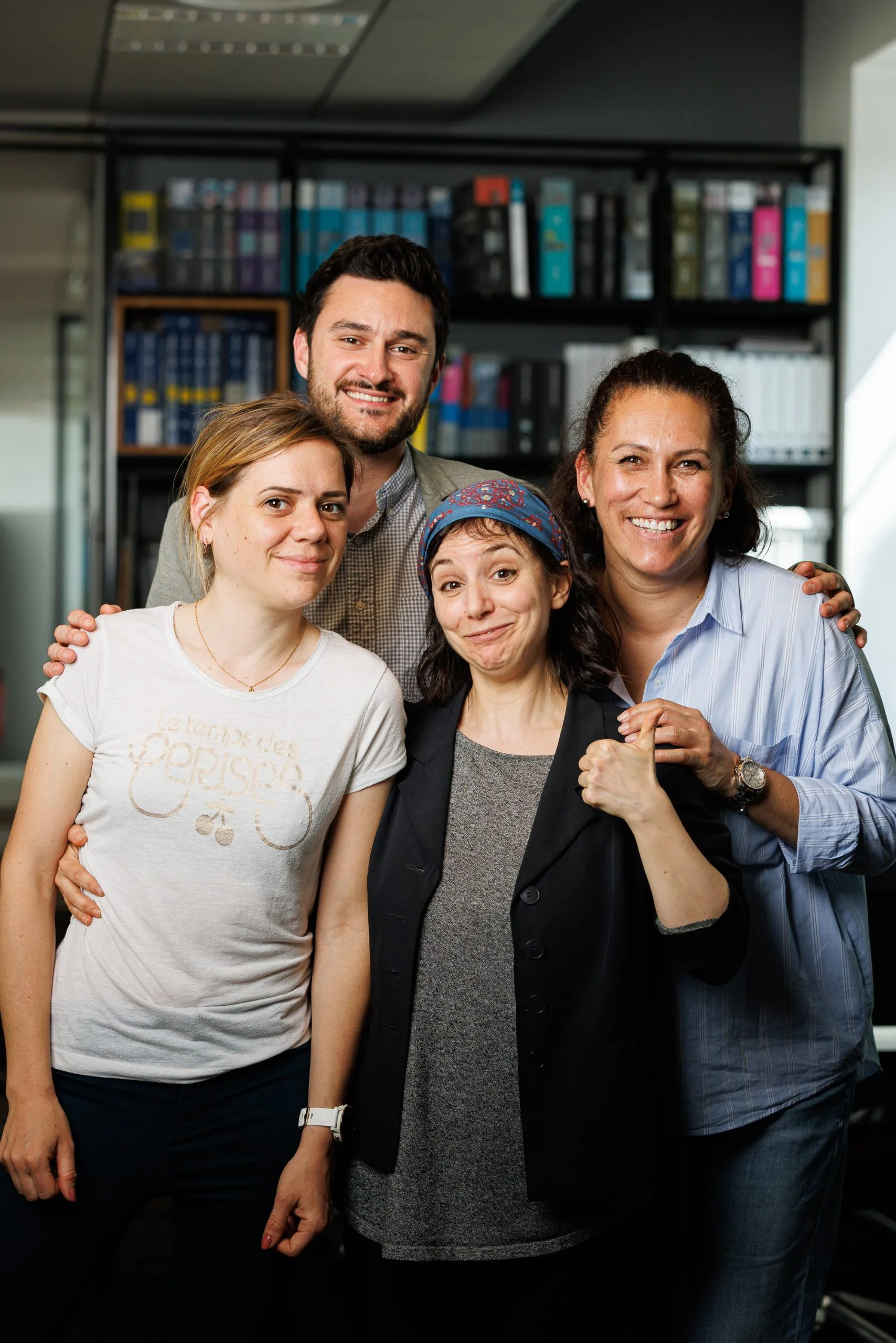 Cinq personnes souriantes posant ensemble dans un bureau avec étagères en arrière-plan.