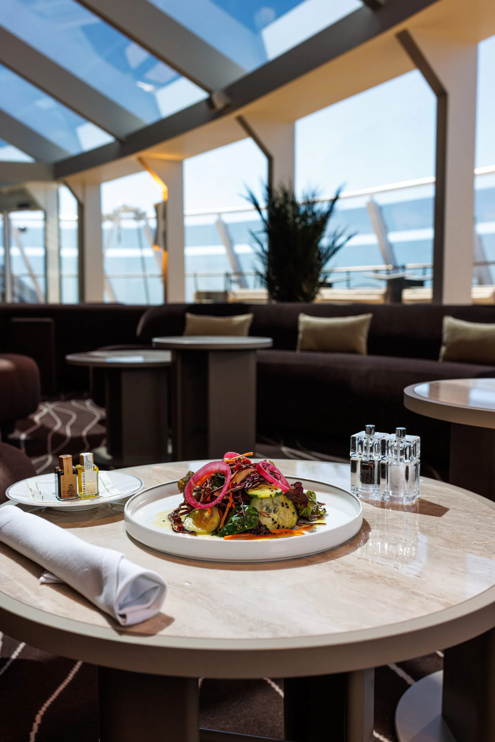 Assiette de salade géante avec des légumes colorés sur une table ronde dans une salle à manger élégante avec vue sur la mer.