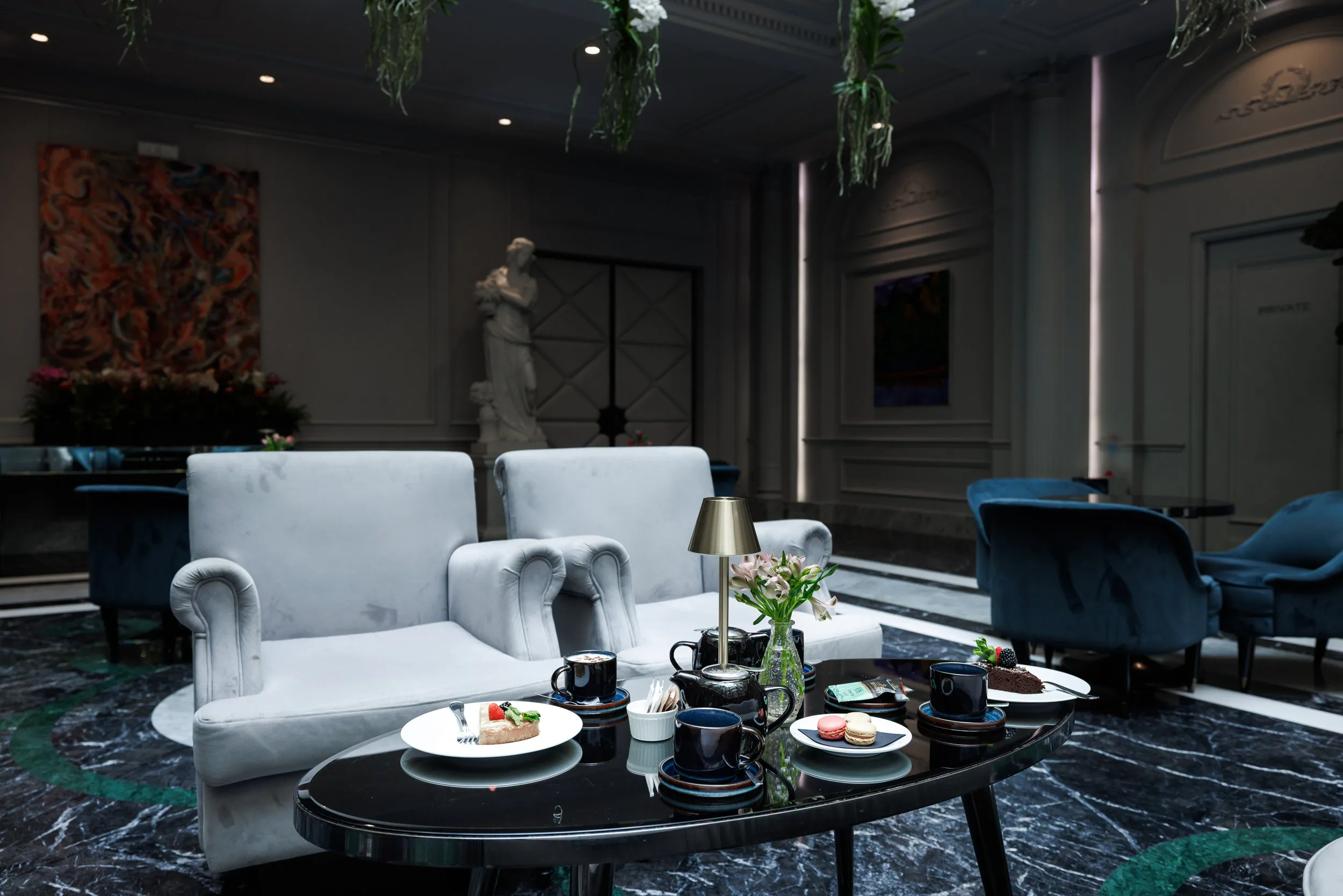 Salon élégant avec canapé blanc, table basse en marbre noir, théières, tasses, assiettes avec des desserts et de la décoration florale.