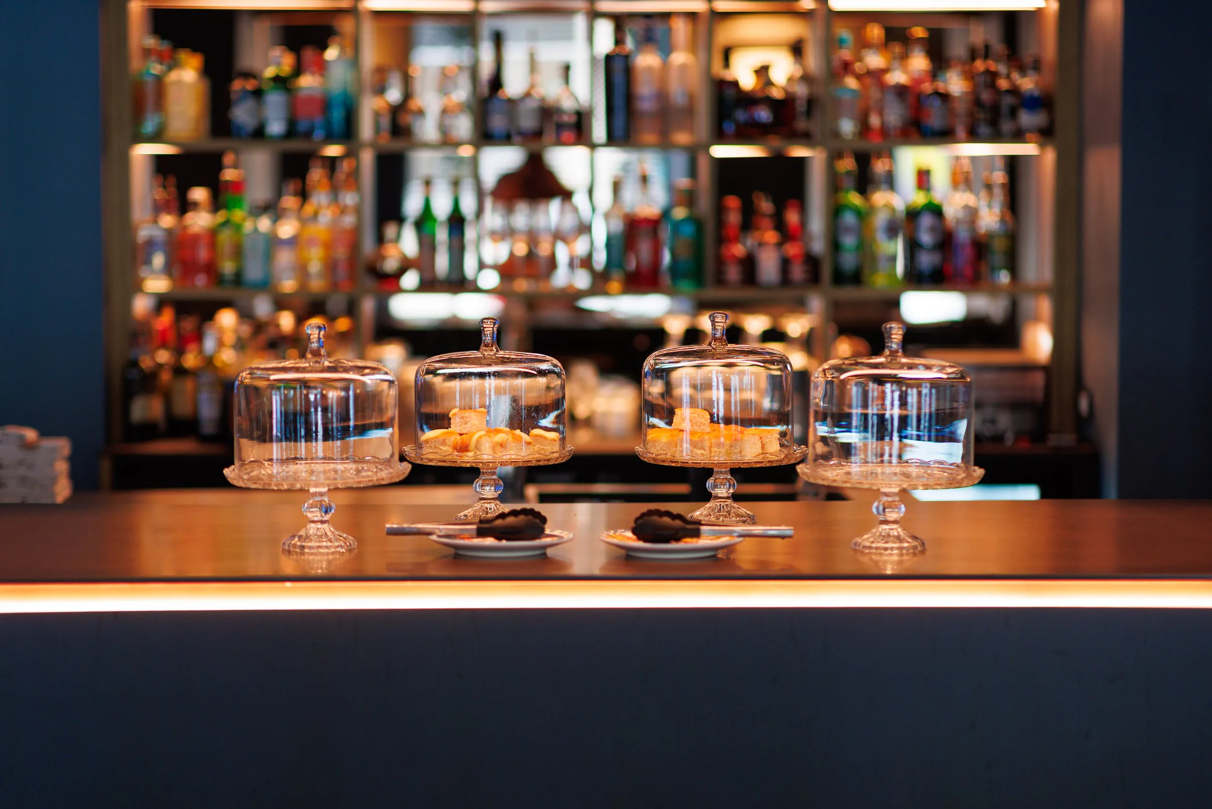 Échantillons de bonbons sous cloche en verre sur un bar, avec une étagère de bouteilles d'alcool en arrière-plan.