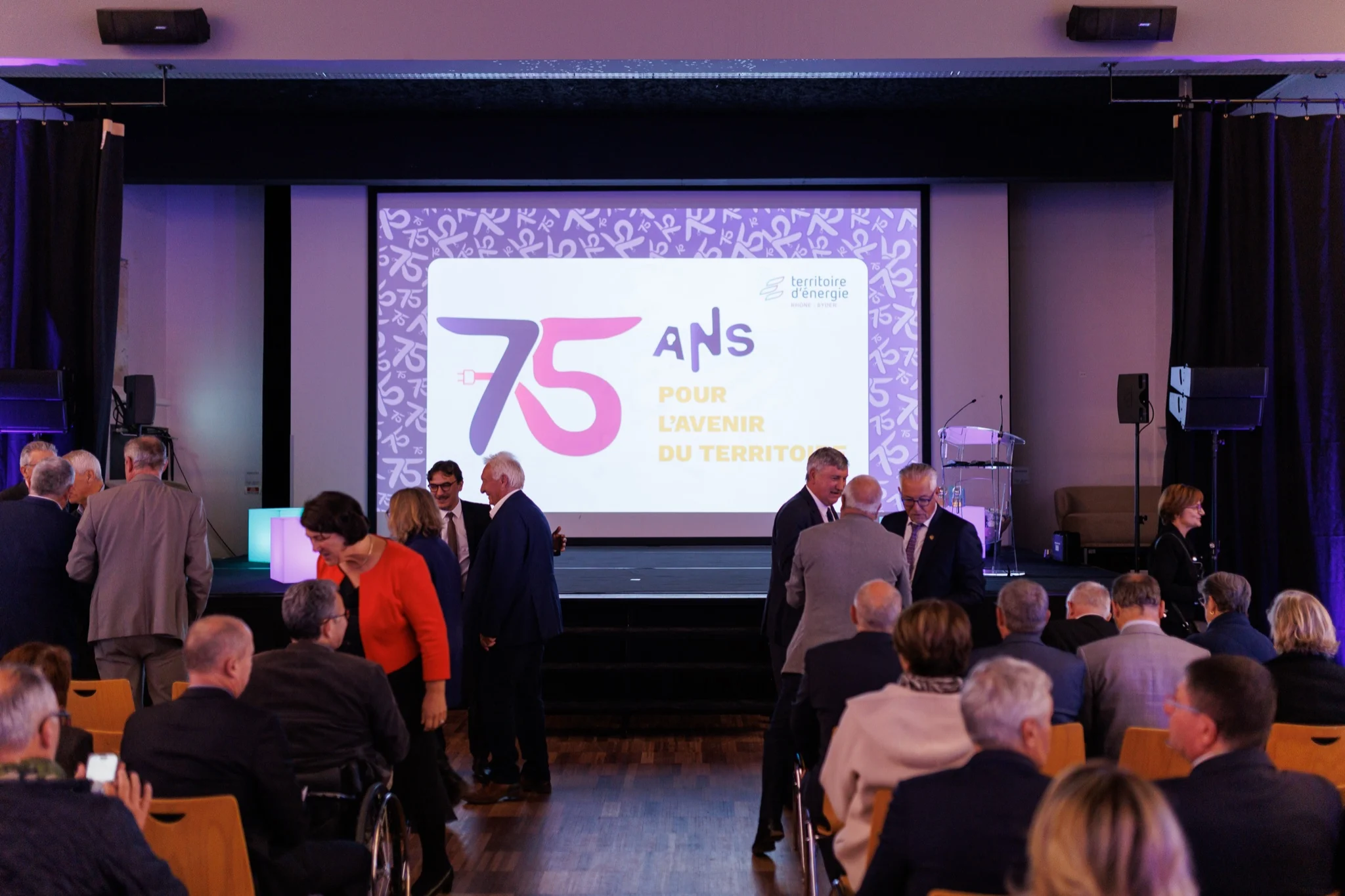 Salle de conférence des 75 ans du SYDER, invités devant l’écran anniversaire