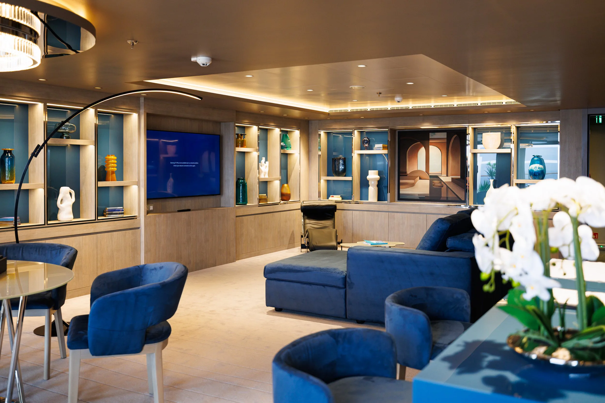 Salon moderne avec fauteuils bleus, table basse, étagères avec des vases et des livres, un mur avec un grand écran de télévision.