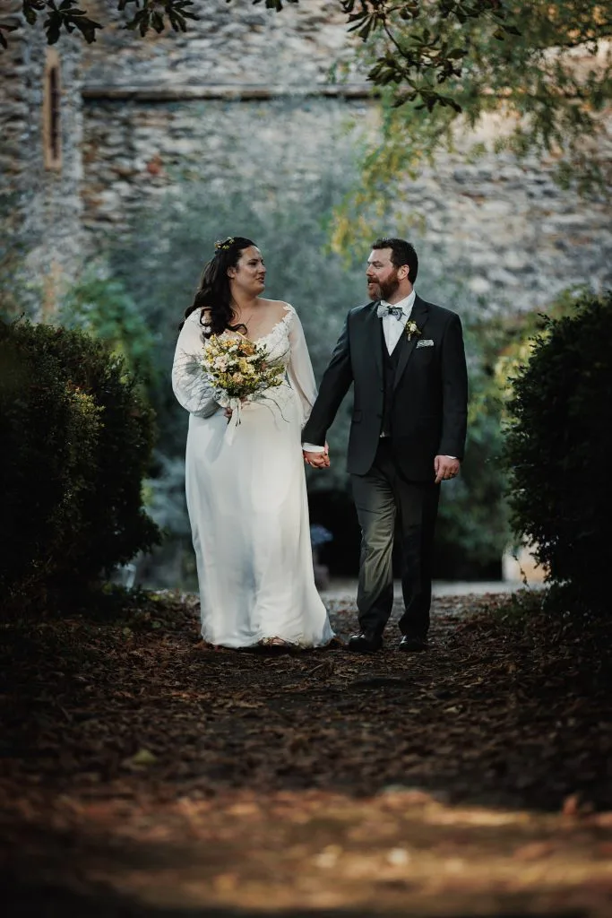 Camille et Jason main dans la main dans une allée ombragée des jardins du château