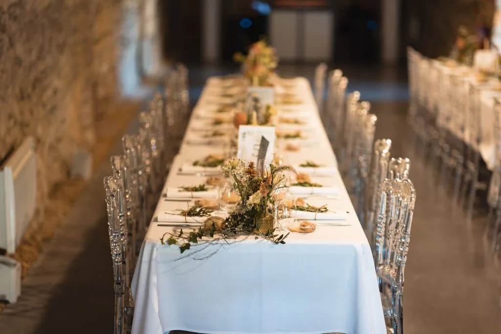 Tables dressées sous la Grande Voûte du Château de Courbeville, chaises transparentes et fleurs