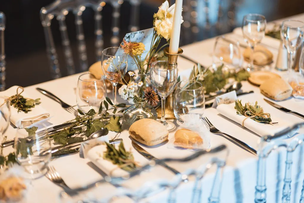 Détail de la table de mariage : fleurs jaunes, pain et verres sur nappe blanche