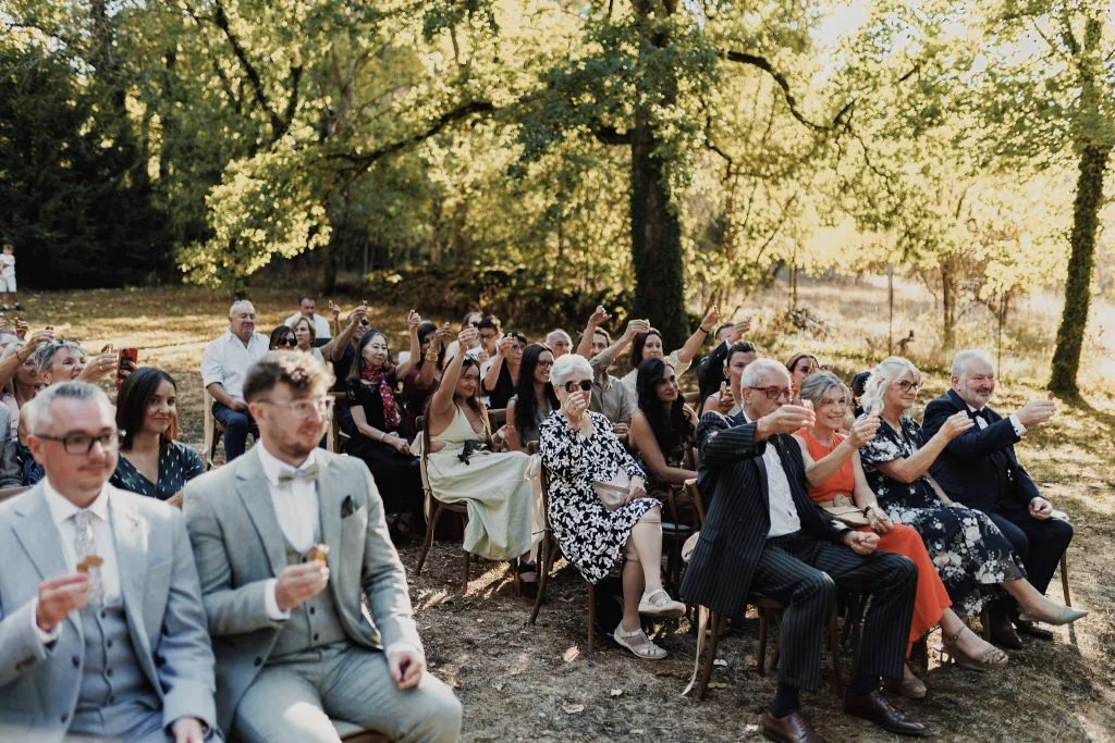 Fin de la cérémonie laïque : les invités, assis dans les jardins, lèvent leur mini-bouteille vers les mariés