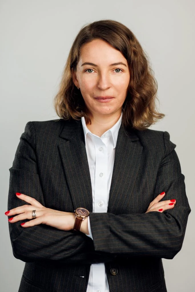 Portrait professionnel d’une femme bras croisés en veste sombre, sur fond gris