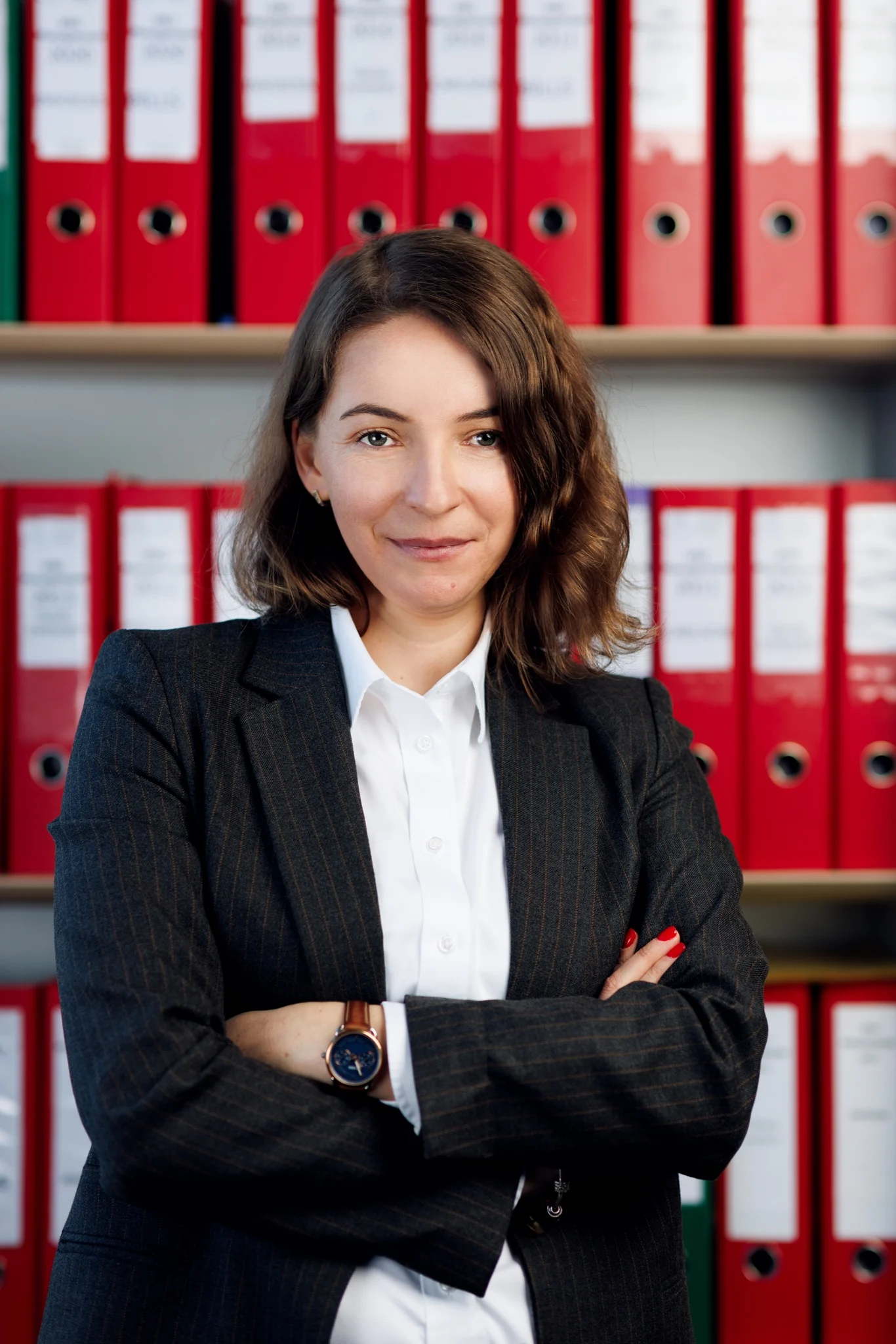 Portrait professionnel bras croisés devant des classeurs rouges, dans un bureau à Lyon